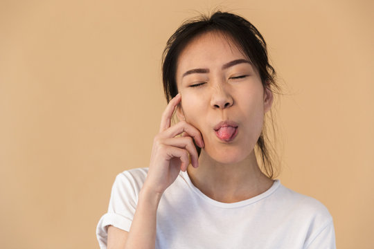 Photo of joyful korean woman wearing basic t-shirt sticking out her tongue and looking at camera