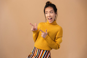 Image of cheerful japanese woman wearing sweater smiling and pointing fingers aside at copyspace