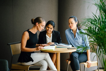 A young Asian Indian woman has a casual business meeting in a meeting room with her team. They sit and use a notebook as their reference for their discussion.