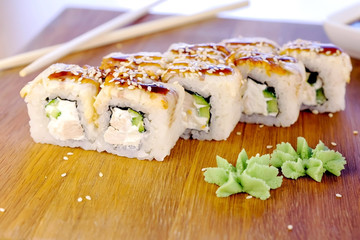 Rolls with fish and sesame seed on top served in wooden board with wasabi, ginger and soy sause