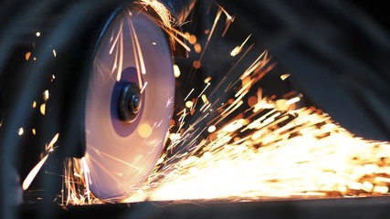 Close-up of worker at construction plant saws metal using circular saw. Industrial production, locksmith industry concept . Sparks from grinding wheel