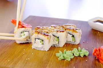 Eats rolls with fish and sesame seed on top served in wooden board with wasabi, ginger and soy sause. Wood sticks close-up