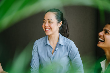 Portrait of a young Eurasian woman manager having a light chat with her team in the meeting room. She is smiling as she talks to her team and is wearing a professional shirt with a collar.