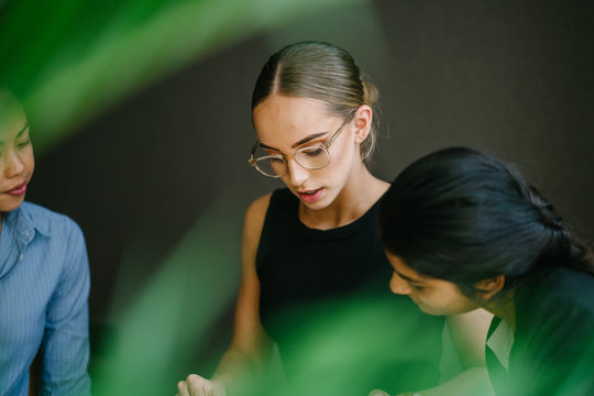 A young Caucasian woman has a casual business meeting with her team. They're sitting down and talking in depth. One of her team mate is Chinese while the other is Indian.