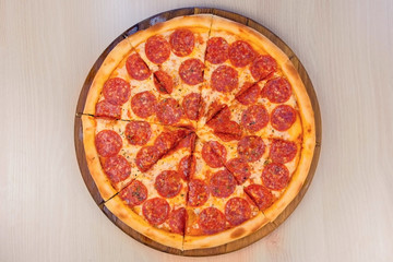 Slicing salami pizza on wooden board on the table. Close-up top view