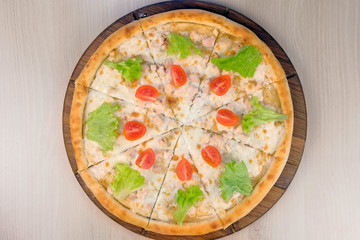 Pizza with chicken and cheese, tomatoes and lettuce on top on wooden board