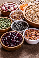 Various assortment set of indian legumes in bowls on wooden background.