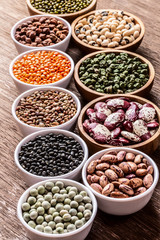 Various assortment set of indian legumes in bowls on wooden background.