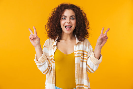 Image of cheerful woman 20s with curly hair smiling and showing victory sign