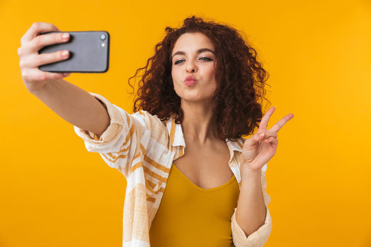 Image of positive woman 20s with curly hair smiling and taking selfie photo on smartphone
