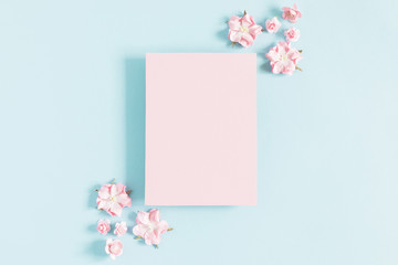 Flowers composition creative. Empty pink paper, flowers on pastel blue background. Flat lay, top view, copy space
