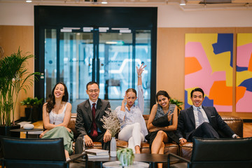 A successful team of young business people at their office. They're all sitting on the couch in front of the camera doing a wacky pose.