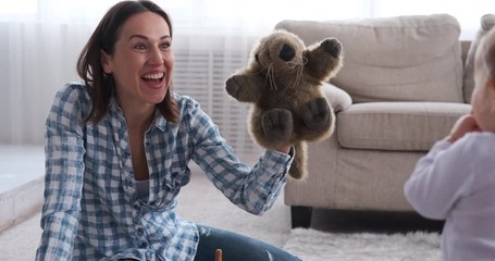 Happy mother and baby daughter playing with toy animal at home