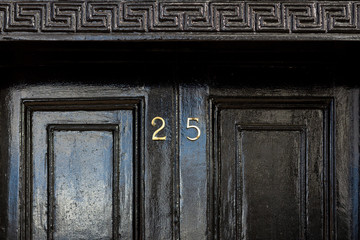 House number 25 in bronze on a black wooden entrance door with the twenty five in bronze and...
