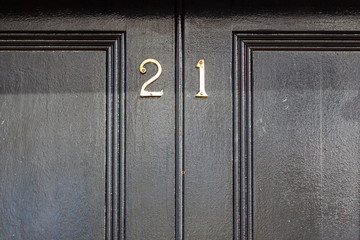 House number twenty one with the 21 in bronze on an elegant panelled black wooden entrance door with recessed panels