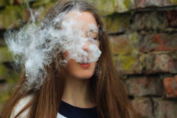 Vape teenager. Young pretty white girl smoking an electronic cigarette opposite destroyed brick wall on the street in the spring. Bad habit.