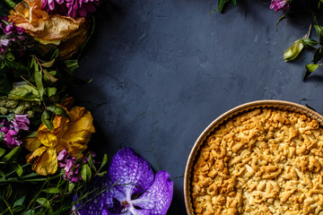 Bouquet of bright flowers and apple pie lying on gray background. Flat lay. Top view