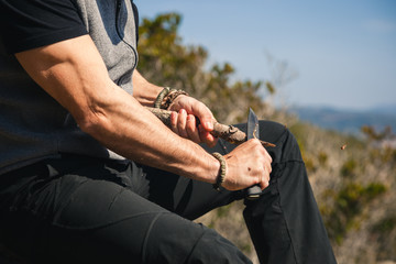 Man sitting on a rock in the nature carving a wooden stick