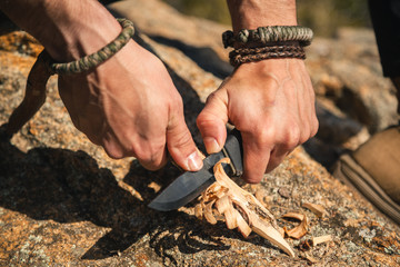 Human hands carving a wooden stick with knife in nature