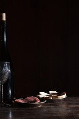 Wine bottle with wineglass and snack in black background