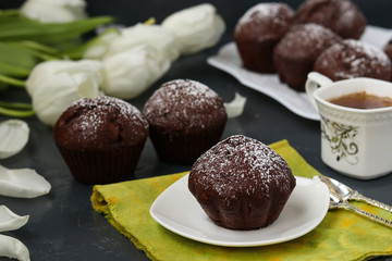 Chocolate muffins with cherry, covered with powder sugar located on a dark background