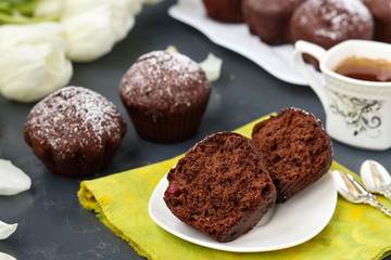 Chocolate muffins with cherry, covered with powder sugar located on a dark background