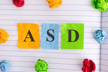 ASD (Autism spectrum disorder) on notebook sheet with some colorful crumpled paper balls around it