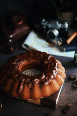 Appetizing chocolate cupcake poured with dark chocolate icing. Near the old book, vintage camera, dominoes.  In the background is an indoor flower and a map of London.