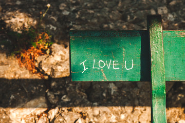 Fragment of green bench in park with handwritten words I Love You. Concept of love, romance, romantic relationship