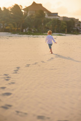 Little boy running along the summer beach with palm trees