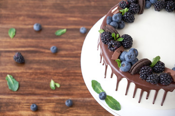 Cake with chocolate, decorated with backberries, blueberries, mint leaves, chocolate bars and cookies on a wooden table. Top view.