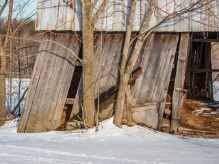 abandoned decaying barn with rusty metal roof in winter beginning to collapse