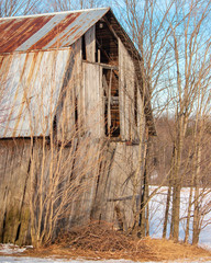 abandoned decaying barn with rusty metal roof in winter beginning to collapse