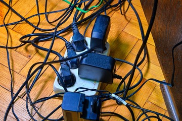 Tangled wires and battery charges on parquete floor. Domestic appliances. Wires mess in domestic...