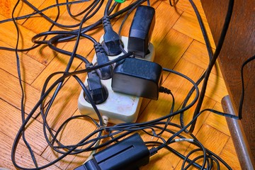 Tangled wires and battery charges on parquete floor. Domestic appliances.  Wires mess in domestic...
