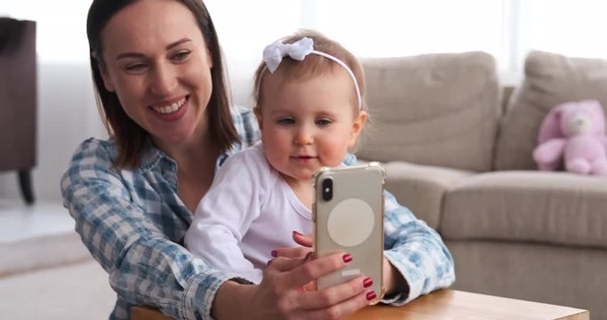Baby girl with mother taking selfie using mobile phone at home