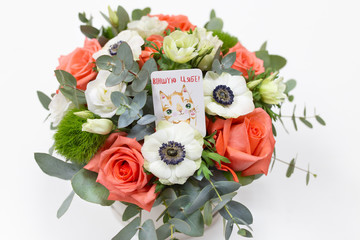 Delicate floral arrangement of roses, anemones (white, pink, orange) and green eucalyptus leaves in a round white cardboard box on a bright background