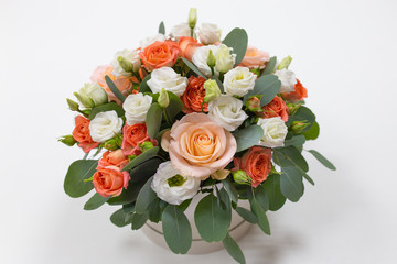 Delicate floral arrangement of roses (white, pink, orange) and green eucalyptus leaves in a round white cardboard box on a light background