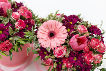 An impressive pairing composition of fresh flowers (Rose, Gerbera, Tulip) (colors: beard, pink, green, white) in a pink cardboard round hat box on a light background