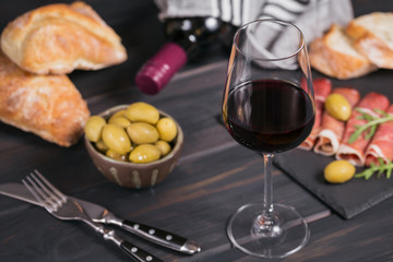 Glass of red wine with slices of cured ham or Spanish jamon serrano or Italian prosciutto crudo, bread, green olives and arugula