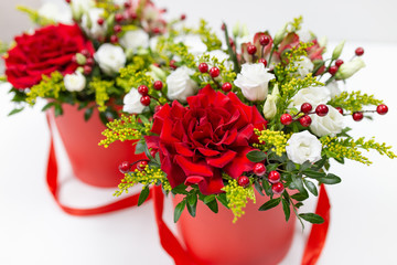Life-affirming composition of fresh flowers (Rose, Eustoma, Solidaga, Pistachio leaves) and decorative berries in a scarlet cardboard round hat box on a light background