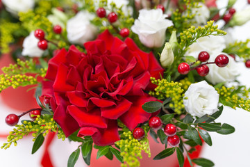 Life-affirming composition of fresh flowers (Rose, Eustoma, Solidaga, Pistachio leaves) and decorative berries in a scarlet cardboard round hat box on a light background