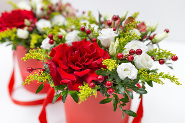 Life-affirming composition of fresh flowers (Rose, Eustoma, Solidaga, Pistachio leaves) and decorative berries in a scarlet cardboard round hat box on a light background