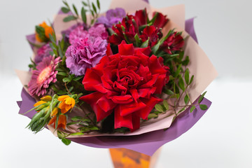 Bright bouquet (red, yellow, green, lilac) of roses, gerberas, alstroemeria and greenery on a light background