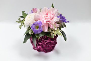 Refined composition of fresh flowers (Rose, Eustoma) and exotic leaves in a burgundy velvet vase on a light background