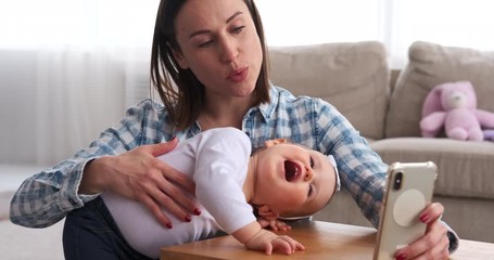 Happy mother with playful baby daughter taking selfie using mobile phone at home