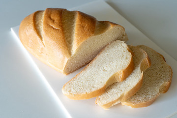 Fresh ruddy long loaf chopped on a white board on a white table. Top view