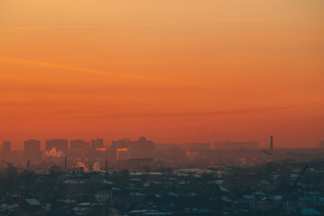Urban high-rise buildings behind private houses on sunset. Silhouettes of big city buildings. Warm backlight of dawn. Private sector near apartment houses in sunlight. Minimalist cityscape at sunrise.