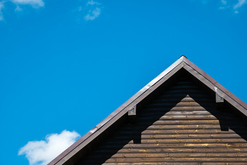 Fragment of triangular roof of modern log house against bright blue sky with white clouds. Copy space