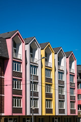 Fototapeta premium Rows of triangular elements of roofline covered with shingle, with chimney against blue sky. Colorful pink and yellow house. Vertical shot